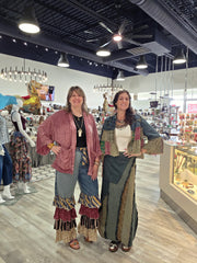 Two women posing in a boutique store, wearing bohemian-style handmade patchwork garments. The woman on the left wears a dusty rose patchwork jacket over a black top and layered Mixed Print Ruffle Flare Pants by Young Threads Robin Boutique ruffle jeans.